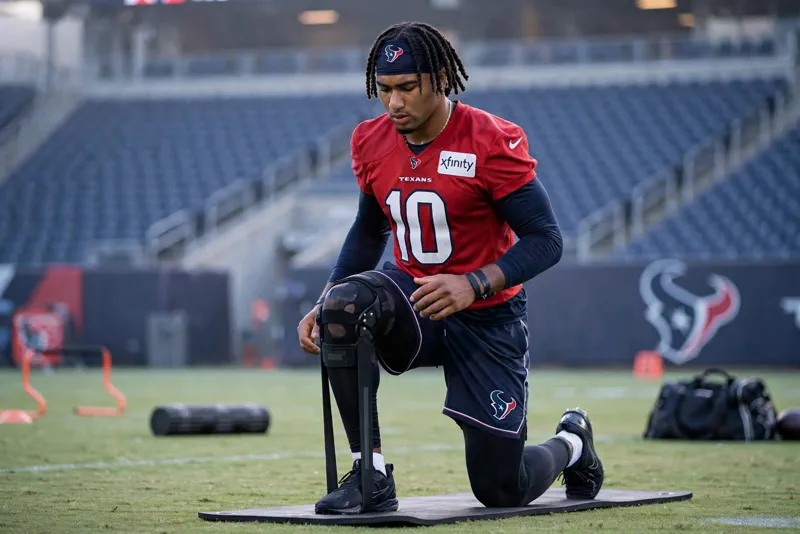Houston Texans wide receiver Tank Dell doing a knee rehabilitation drill on a practice field at dawn, symbolizing his long comeback from a devastating injury