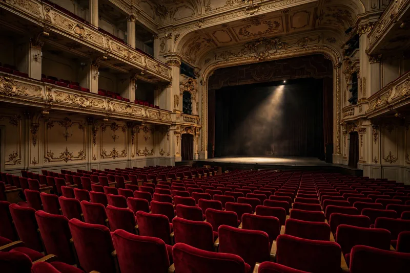 An empty grand concert hall with rows of red seats facing a darkened stage