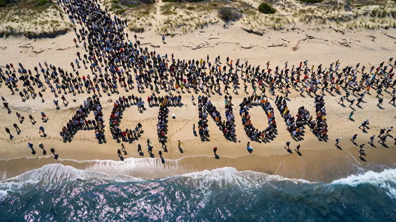 Aerial view of a large group of people on a beach forming a message with their bodies on a sunny day